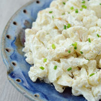 cauliflower potato salad sprinkled with chives in a blue ceramic dish