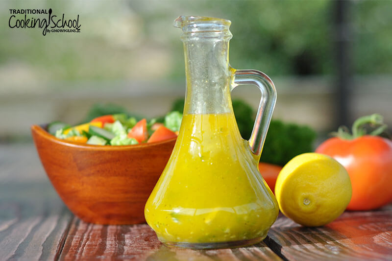 small dressing bottle full of a lemon vinaigrette with a bowl of salad behind it