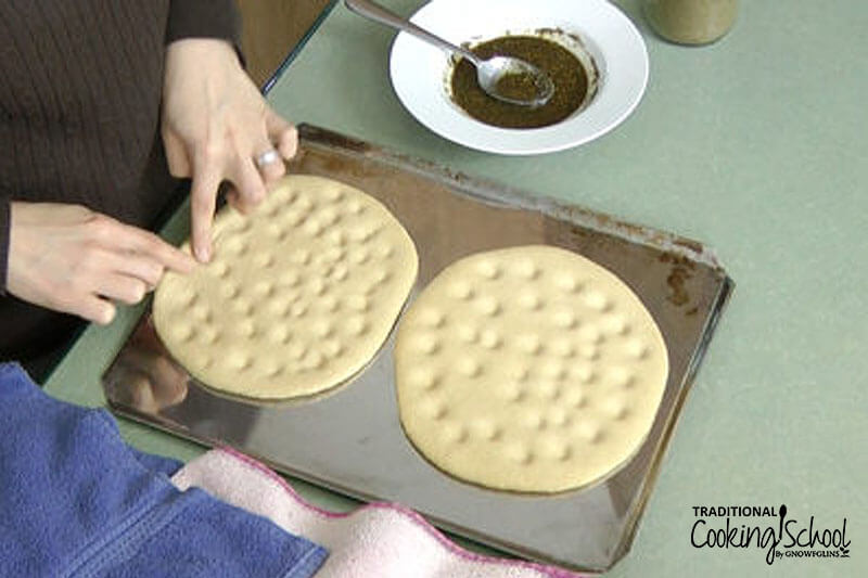 Manakish dough being pressed with fingers before baking.
