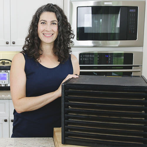 woman smiling in kitchen next to a 9-tray vertical food dehydator