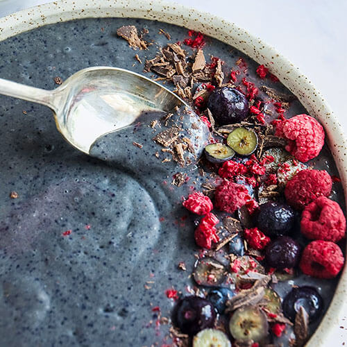 blue-purple smoothie bowl garnished with raspberries, blueberries, and shaved chocolate