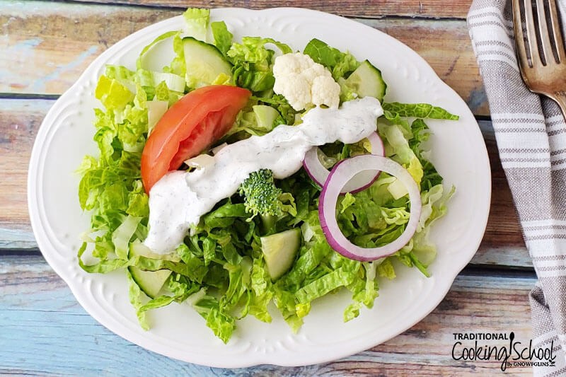 Green salad on a plate with fresh veggies and a drizzle of creamy homemade salad dressing on top.