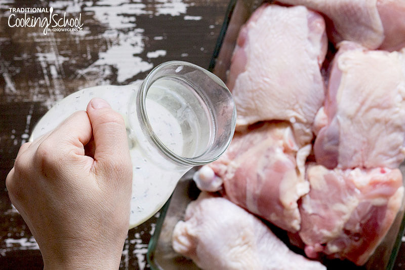 woman's hand pouring salad dressing over pieces of chicken to marinate