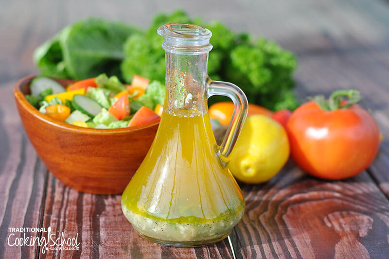 small pitcher of a lemon vinaigrette in front of produce and a green salad