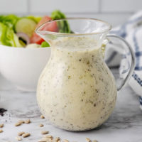 pitcher of creamy, light-colored dressing with black specks in front of a green salad