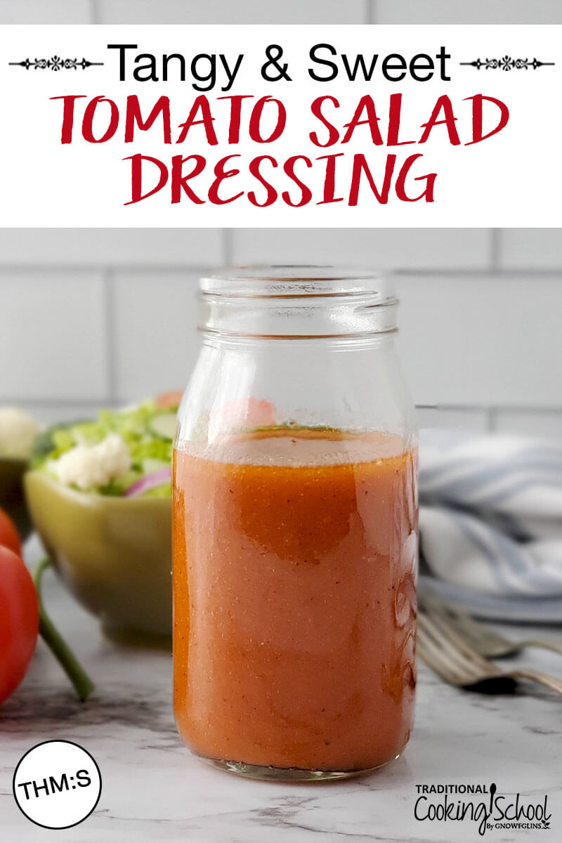 small glass jar of rust-colored vinaigrette with fresh green salad in the background and text overlay: "Tangy & Sweet Tomato Salad Dressing (THM:S)"
