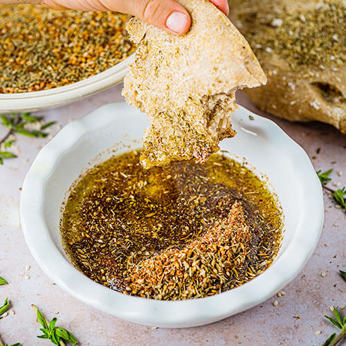 dipping a piece of flatbread in a bowl of zatar and olive oil