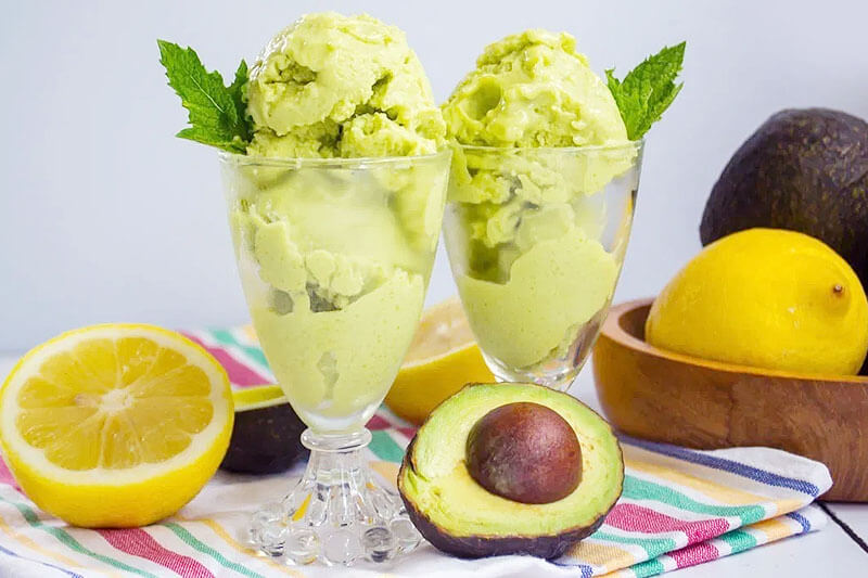 green ice cream in two decorative dishes with avocados and lemons surrounding