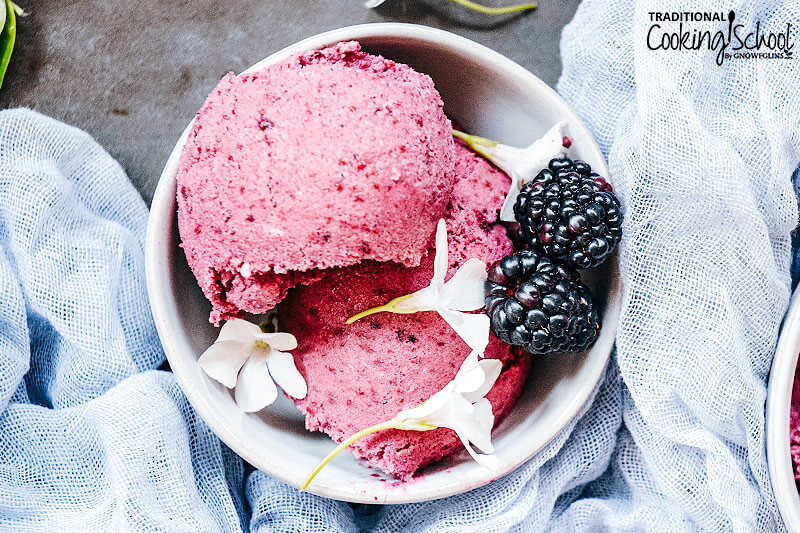 bright pink ice cream in a bowl garnished with blackberries and blossoms