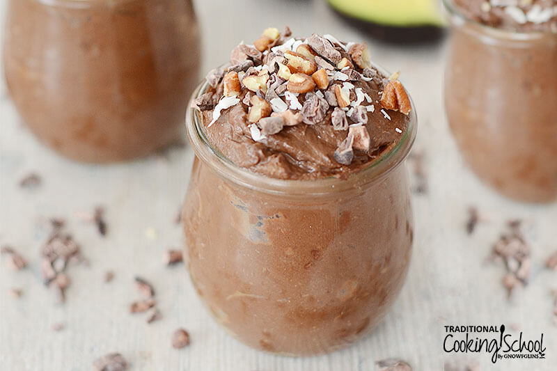 chocolate avocado mousse in a small glass cup garnished with nuts and cacao nibs