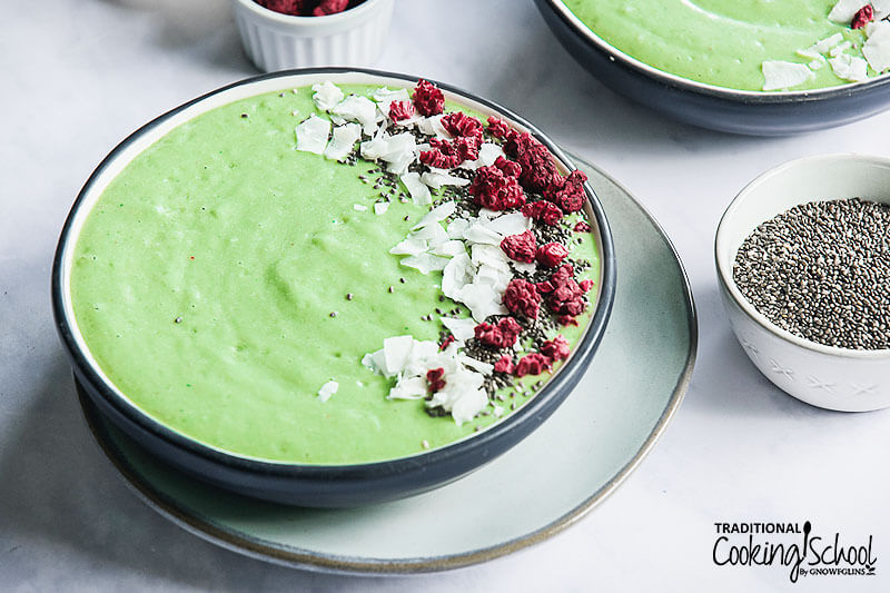 bright green smoothie bowl garnished with coconut, freeze-dried raspberries, and chia seeds