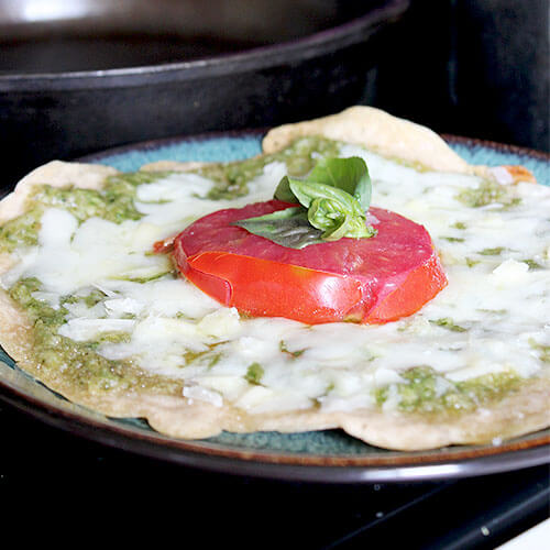 mini pizza on a plate topped with pesto, melted mozzarella, fresh tomato and basil