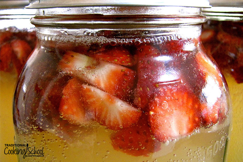 glass jar of water kefir flavored with fresh strawberries