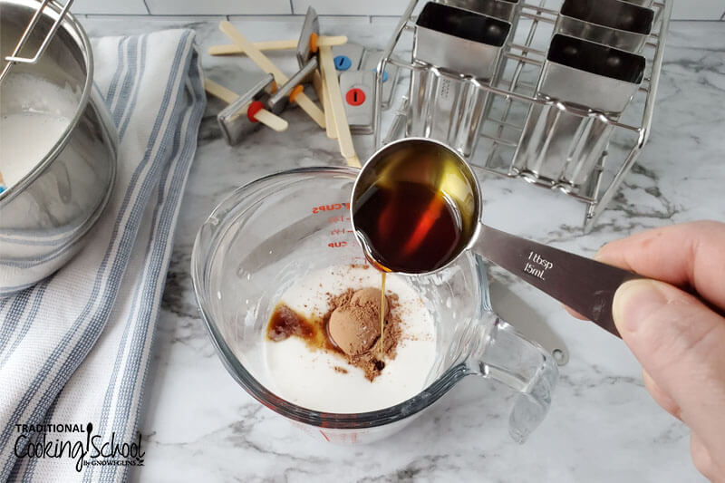 woman's hand pouring a teaspoon of vanilla extract into a measuring glass of other ingredients