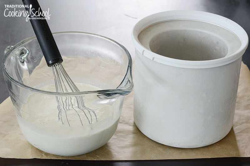 large glass bowl of vanilla ice cream filling and a whisk, next to an ice cream maker