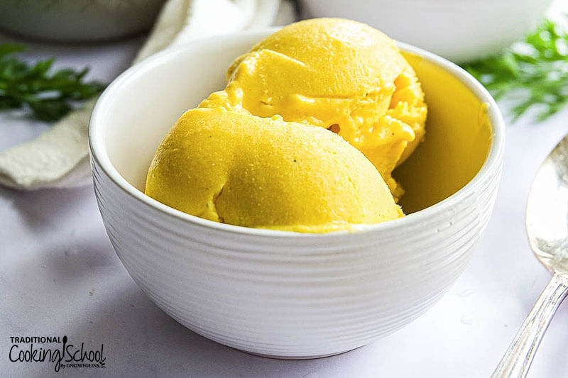 white ceramic bowl of bright yellow-colored scoops of ice cream