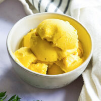 white ceramic bowl of bright yellow-colored scoops of ice cream