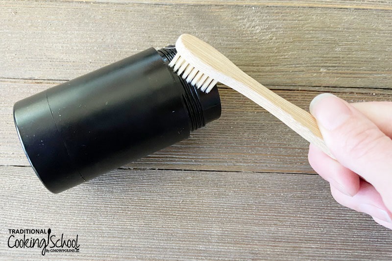 Woman's hand scrubbing out a deodorant stick with a toothbrush to re-use for homemade deodorant.