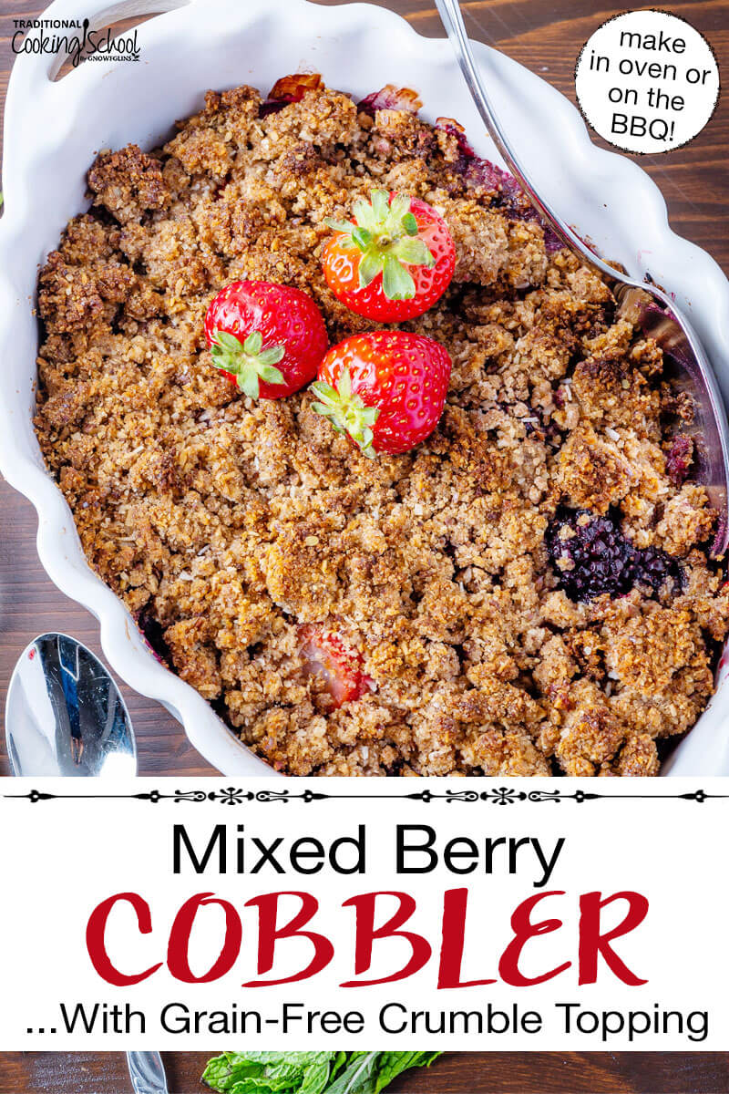 Cobbler garnished with fresh strawberries, in a white casserole dish with scalloped edges. Text overlay says: "Mixed Berry Cobbler ...With Grain-Free Crumble Topping (make in oven or on the BBQ!)"