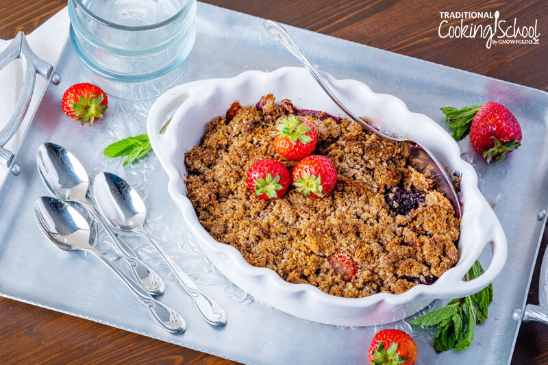 Gluten-free cobbler in a white ceramic dish with scalloped edges, garnished with fresh strawberries.