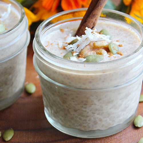 close-up shot of a small 1/2 pint jar of chia seed pudding, topped with a cinnamon stick, sprinkle of cinnamon, shredded coconut, and pumpkin seeds