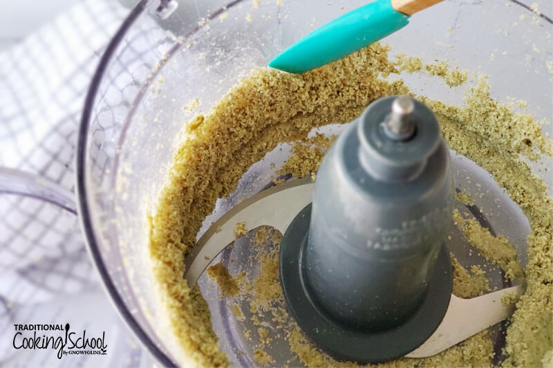 spatula scraping down the sides of a food processor when making pumpkin seed butter