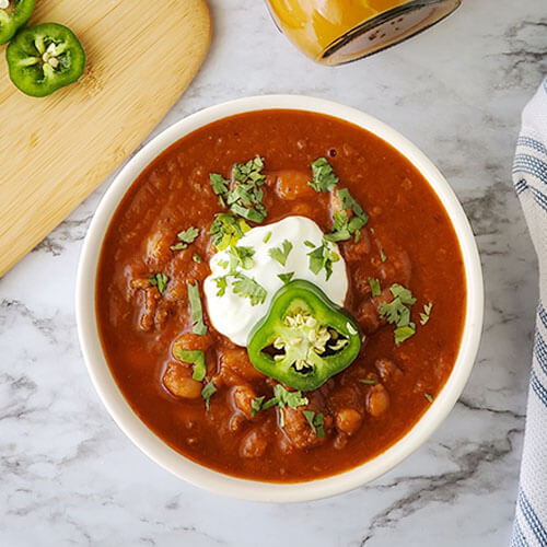 A bowl of chili garnished with fresh herbs, sour cream, and a slice of pepper.