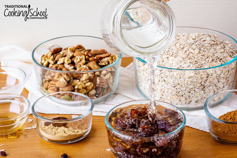 Pouring water into a bowl of dates, with bowls of other ingredients in the background: spices, oats, nuts and seeds.