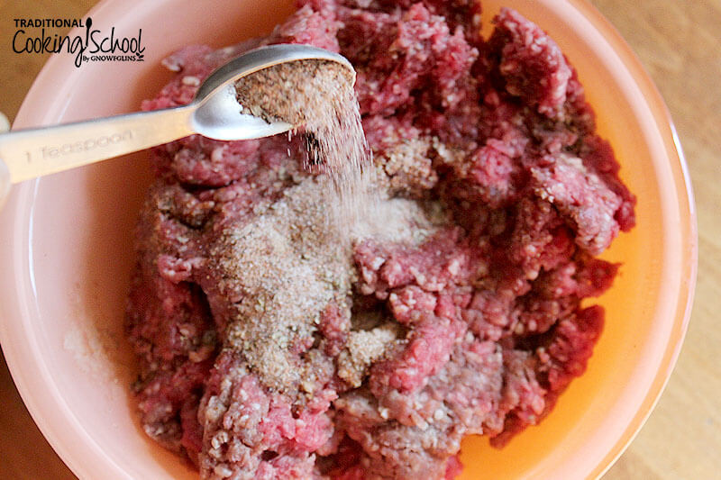 Teaspoon sprinkling spices onto ground beef in a bowl.