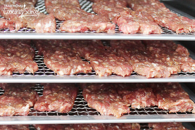 Strips of raw meat on dehydrator trays ready to be turned into homemade jerky.