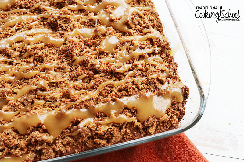 Coffee cake in a glass cake pan topped with crumb topping and vanilla icing drizzle.
