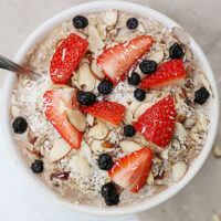 Bowl of muesli topped with fresh strawberries, blueberries, slivered almonds, and shredded coconut.