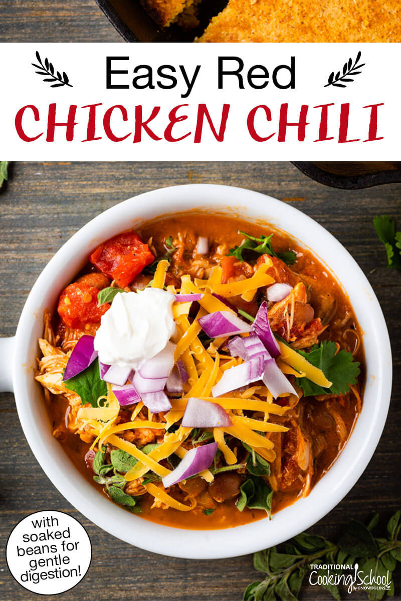 Bowl of chili topped with sour cream, red onion, cilantro, and grated cheddar cheese. Text overlay says: "Easy Red Chicken Chili (with soaked beans for gentle digestion!)"