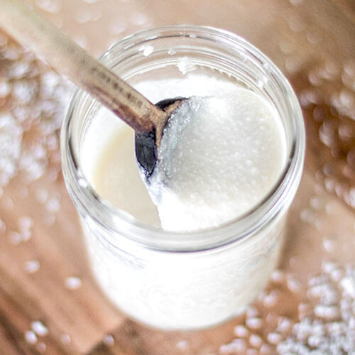 Jar of creamy coconut butter with a wooden spoon scooping some out.