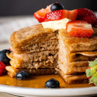 Stack of sourdough pancakes on a plate topped with fresh fruit, butter, and syrup.