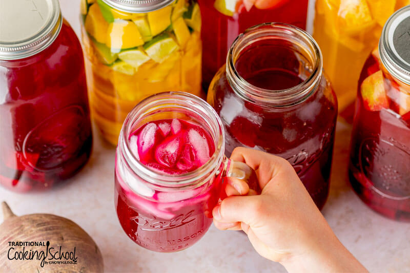 Holding up a glass jar of beet kvass with ice cubes.
