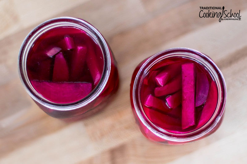 Overhead shot of two quart-sized glass jars of pickled turnip and beet slices which have turned a deep burgundy color.
