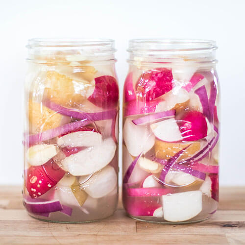 Radishes pickling in quart-sized Mason jars along with other red onion slices.