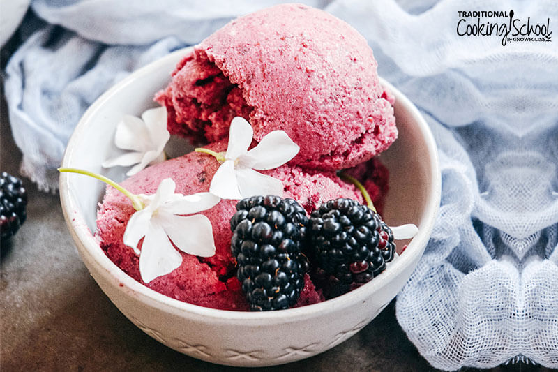 Blackberry ice cream in a small dish garnished with blackberries and white blossoms.