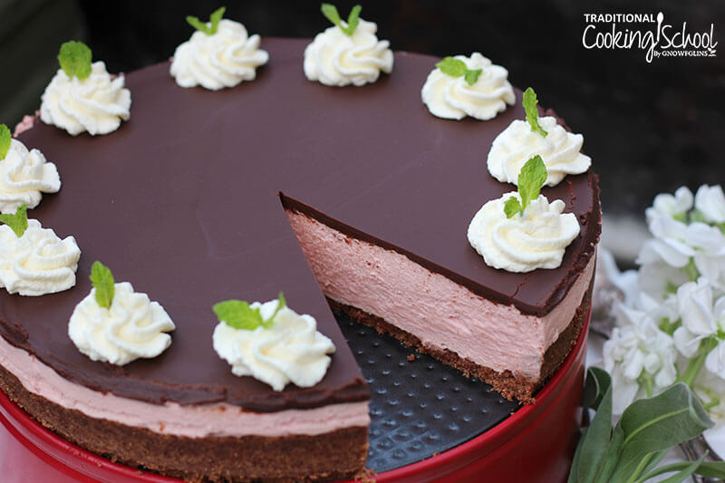 No-bake peppermint cheesecake with a slice taken out of it, garnished with dollops of whipped cream and mint leaves.