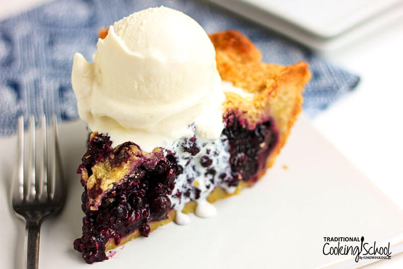 Slice of blueberry pie with a scoop of vanilla ice cream on top.