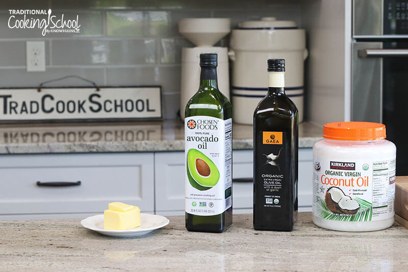 Array of healthy, traditional fats on a countertop: butter, avocado oil, olive oil, and coconut oil.