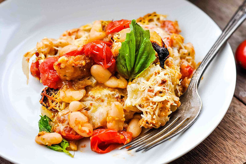Cheesy tomato casserole with beans, topped with fresh basil.