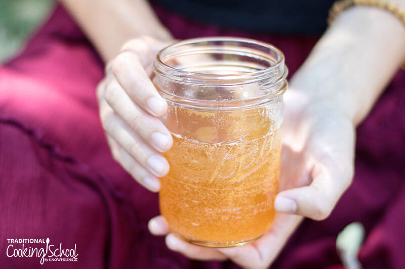Woman's hands holding a glass jar of fizzy, fermented apple cider.