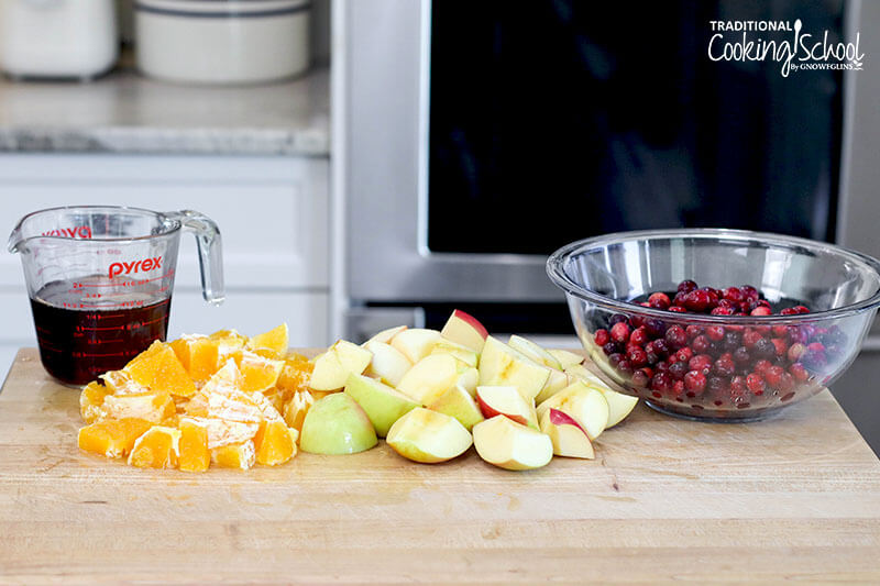 Ingredients for homemade cranberry orange relish: maple syrup, oranges, apples, and fresh cranberries.