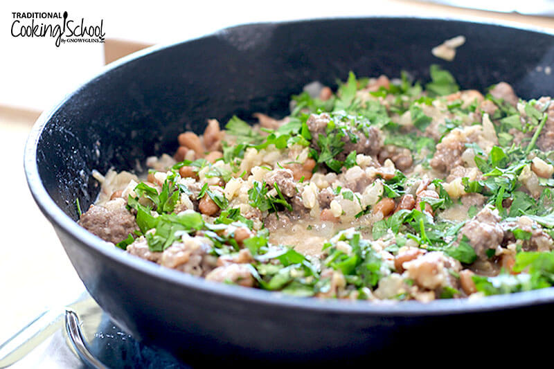 Skillet dish of rice, beef, and beans garnished with fresh herbs.