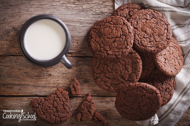 Chocolate gingersnap cookies on a wooden table next to a glass of milk.